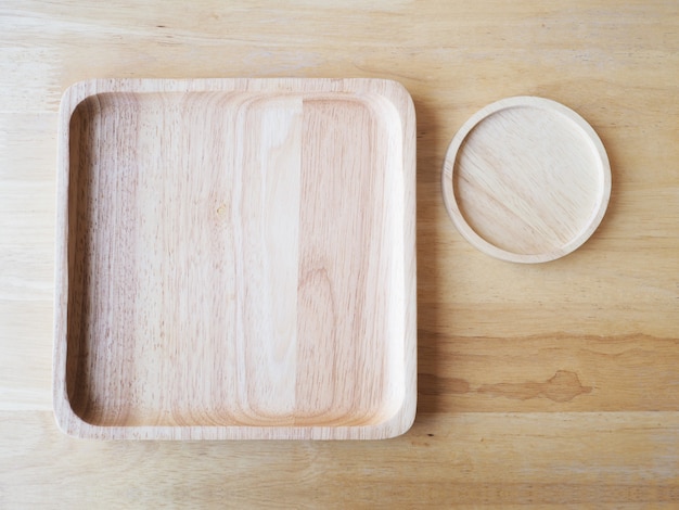 Drewniane kwadratowe i okrągłe talerze na tle drewna