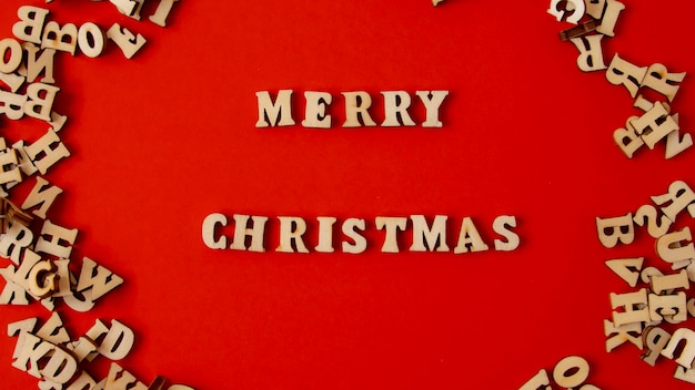 Drewniane litery na ciemnoczerwonym tle napisane po angielsku „Wesołych Świąt”