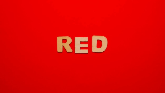 Drewniane litery na jednolitym kolorowym tle ze słowem napisanym w języku angielskim Red