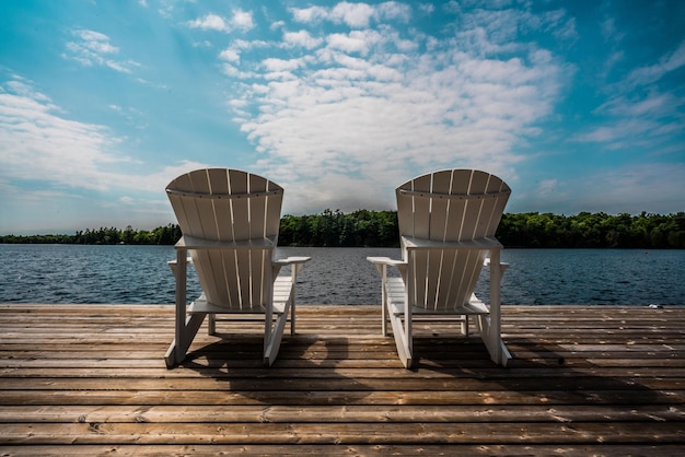Zdjęcie drewniane molo z białymi krzesłami z widokiem na jezioro i zielony las