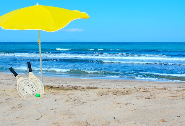 Drewniane rakiety plażowe i żółty parasol nad morzem