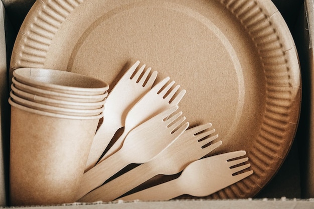 Drewniane widelce i papierowe kubki z talerzami na papierowym tle Kraft Ekologiczna jednorazowa zastawa stołowa