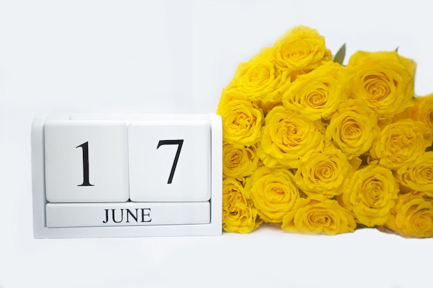 Drewniany biały kalendarz 17 czerwca leżą obok niego bukiet żółtych róż