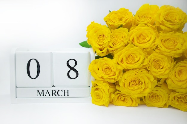 Drewniany, biały kalendarz 8 marca i żółte róże na białym tle, wydarzenie, urodziny, pocztówka, tex
