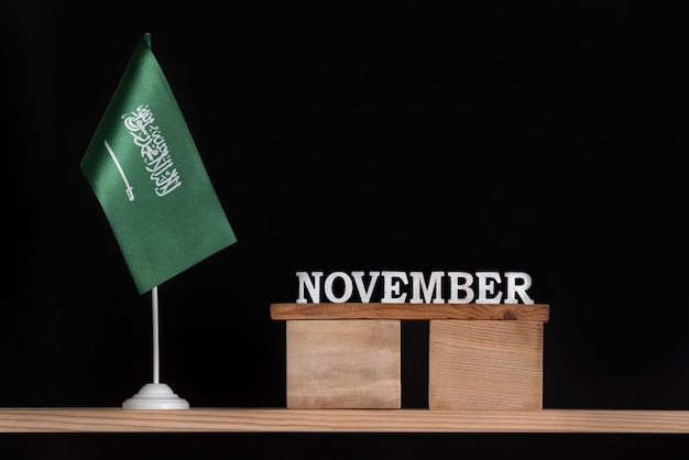Drewniany kalendarz listopada z flagą Arabii Saudyjskiej na czarnym tle. Daty Arabii Saudyjskiej w listopadzie.