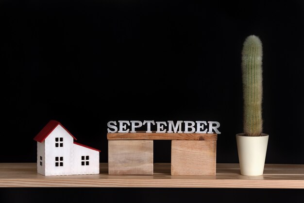 Zdjęcie drewniany kalendarz września, model kaktusa i domu na czarnym tle. skopiuj miejsce.