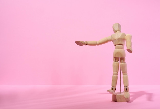 Drewniany kukiełkowy mężczyzna na różowym tle, wskazując ręką