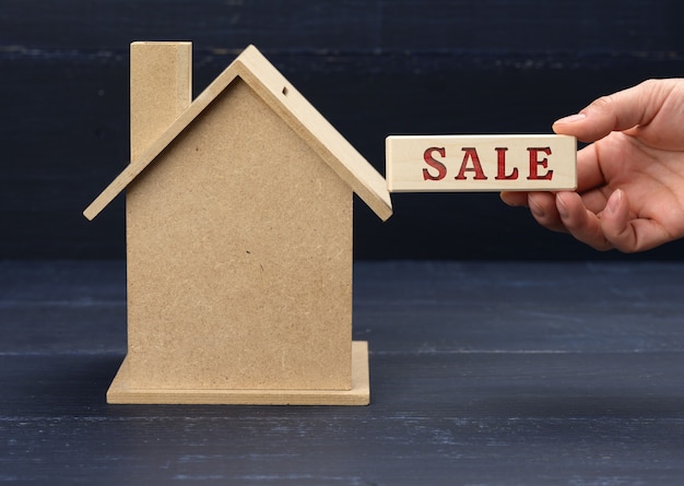 Zdjęcie drewniany model domu i ręka trzyma klocek z napisem sprzedaż na niebieskiej powierzchni
