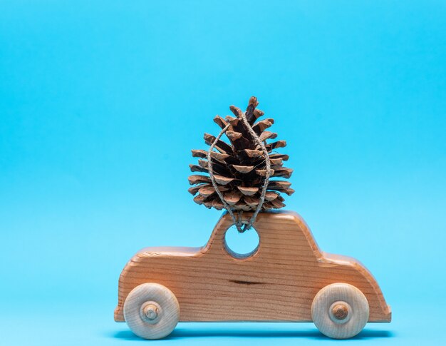 Drewniany samochodzik nosi na wierzchu stożek sosnowy