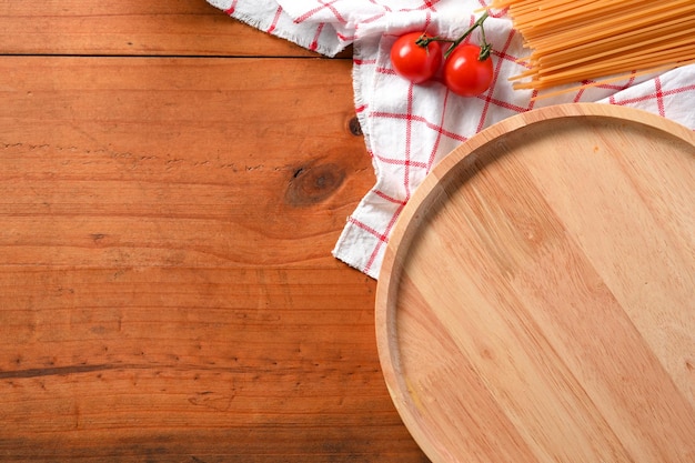 Drewniany stół jadalny z miejscem na kopię na okrągłym drewnianym talerzu świeże pomidory i surowe spaghetti