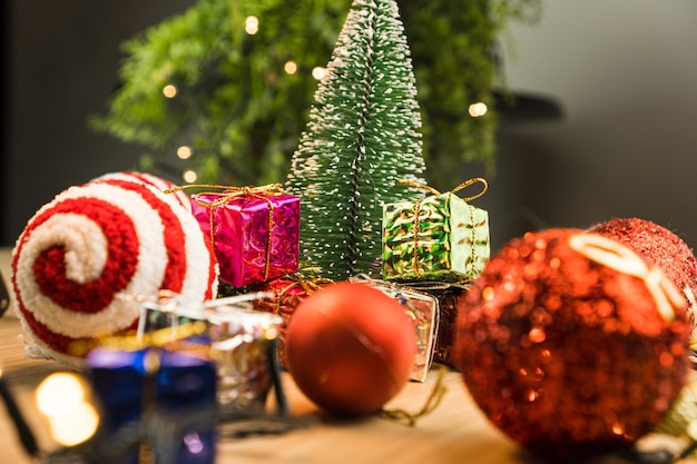 Drewniany stół z dekoracjami świątecznymi. Kule czerwone, srebrne i złote, pudełka na prezenty, lampki, choinki i inne. Selektywne skupienie.