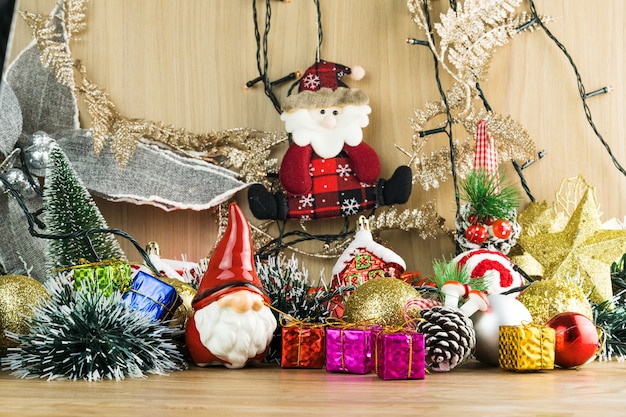 Drewniany stół z dekoracjami świątecznymi. Kule czerwone, srebrne i złote, pudełka na prezenty, lampki, Mikołaj, Panettone, choinka i inne. Selektywne skupienie.
