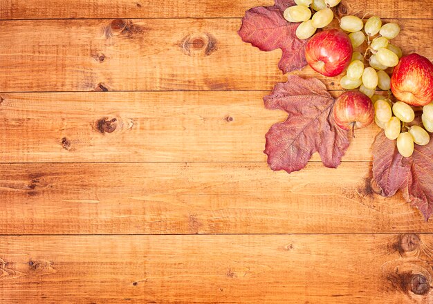 drewniany stół z kompozycją jesiennych liści, jabłek i winogron. Widok z góry
