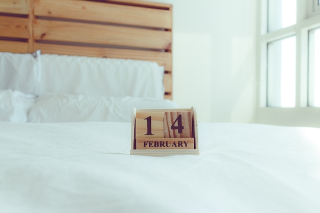 Drewniany sześcian z tekstem 14 lutego na białym łóżku w koncepcji Walentego.