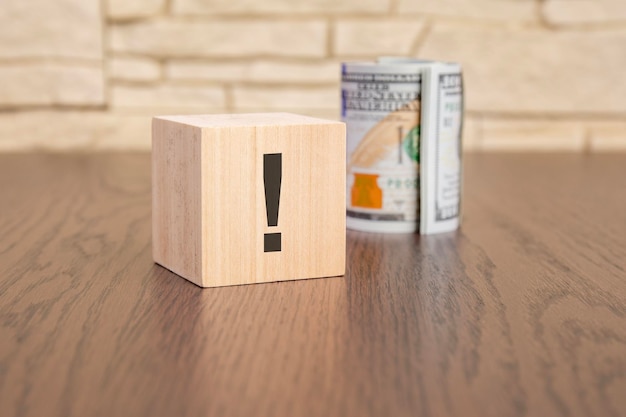 Drewniany sześcian z wykrzyknikiem i banknoty dolarów na drewnianym stole koncepcja niepewności często zadawane pytania i odpowiedzi