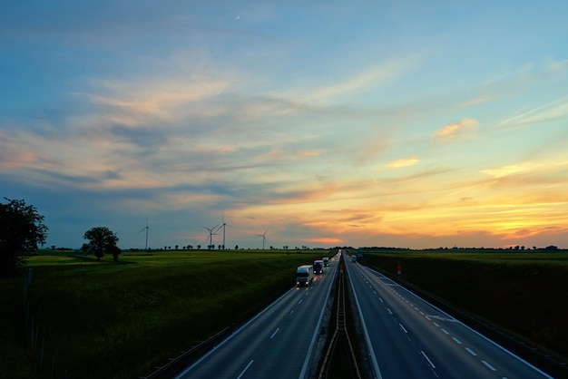 Droga autostradowa z ruchem samochodowym i generatorem turbin wiatrowych na tle zachodu słońca koncepcja czystego ren