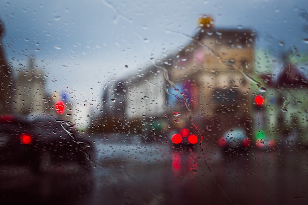 Droga miejska widziana przez krople deszczu na przedniej szybie samochodu
