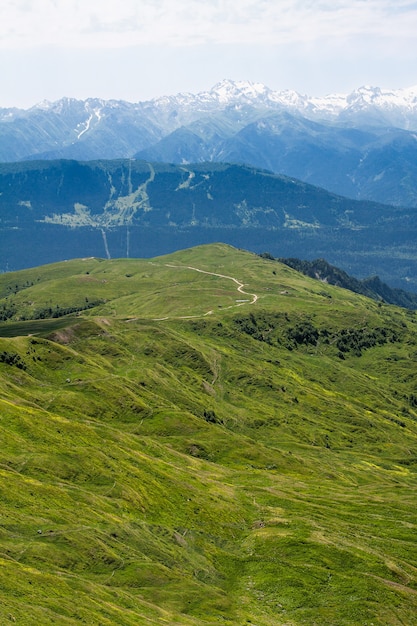 Droga na szczyt górskich wiatrów wzdłuż zielonej równiny na tle błękitnych gór i chmur