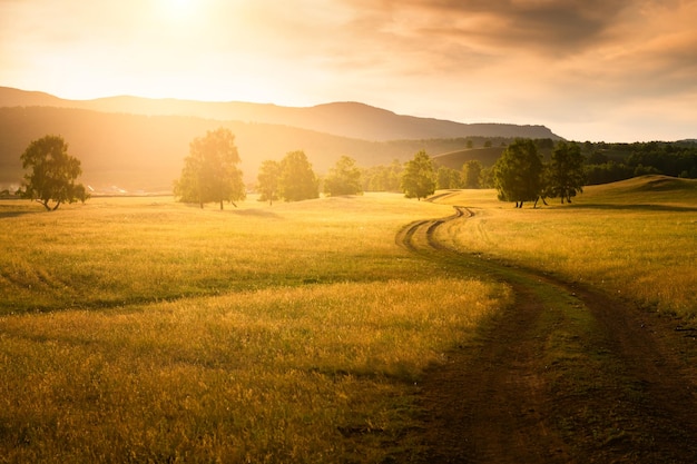 Droga na wsi o zachodzie słońca. Pola z zieloną trawą, lasem i górami. Piękny letni krajobraz. Baszkortostan, Ural Południowy, Rosja
