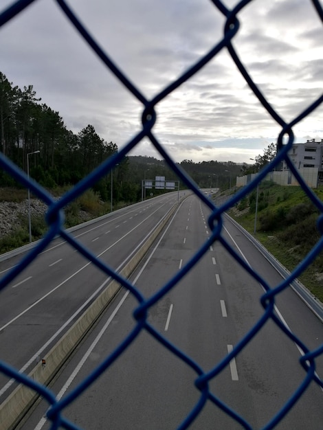 Zdjęcie droga widziana przez ogrodzenie łańcuchowe na tle nieba