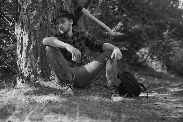 Drwal pracownik mężczyzna siedzi w lesie drwal z siekierą na tle lasu mężczyzna robi mans