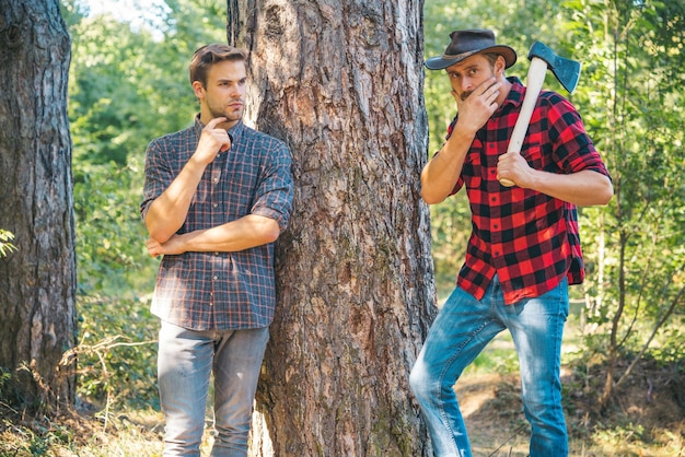 Drwale Drwale Hipsterzy mężczyźni na poważnej twarzy z siekierą Drwal brutalny i brodaty trzyma siekierę Dwóch drwali w lesie Mężczyzna w kapeluszu wygląda brutalnie