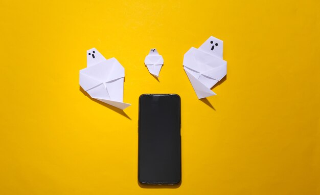 Duchy origami i smartphone na żółtym jasnym tle. Widok z góry