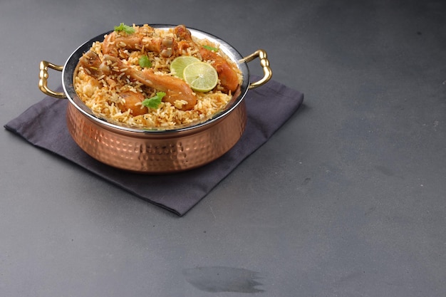 Dum chicken biriyani, zbliżenie Kerala-Thalassery biriyani, które jest zmieszane z masala i żółtym kolorem, ułożone w miedzianej misce do serwowania i przyozdobione plasterkami cytryny umieszczonymi na graficie