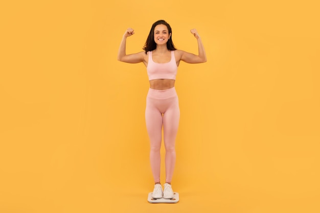 Dumna młoda fitness dama stojąca na wagach pokazująca studio bicepsów