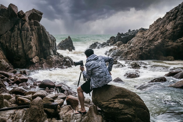 Dumny Fotograf W średnim Wieku, Trzymający Aparat Fotograficzny, Statyw I Stojący W Obliczu Burzy Na Brzegu Morza