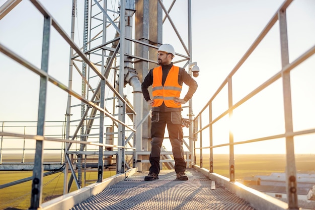 Dumny pracownik wysokościowy stoi na szczycie metalowej konstrukcji i patrzy na horyzont