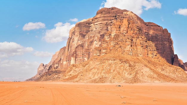 Duża góra na czerwonej pustyni, mały pojazd z napędem na cztery koła na pierwszym planie dla skali - typowa sceneria Wadi Rum, Jordania