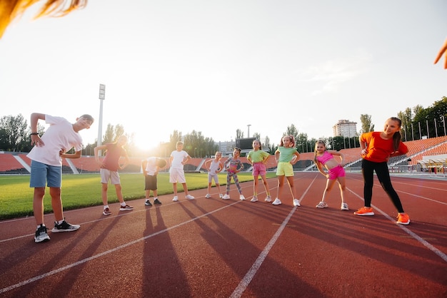 Duża grupa dzieci chłopców i dziewczynek rozgrzewa się i trenuje pod okiem trenera na stadionie podczas zachodu słońca Zdrowy styl życia