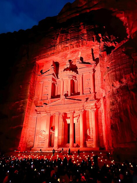 Duża grupa ludzi siedzących na ziemi w nocy, wykuta w skale architektura Al Khazneh lub The Treasury w Petra Jordan