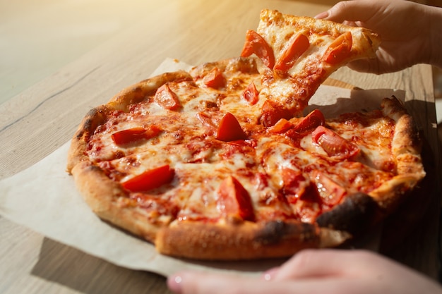 Duża pizza stoi na stole w kawiarni z bliska. Włoska pizza pokrojona na kawałki.
