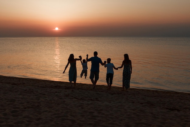 Duża rodzina na plaży. Sylwetki ludzi przed zachodem słońca. 5 osób trzymających się za ręce