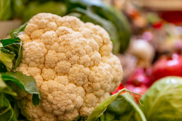 Duża świeża głowa kalafiora na ladzie z warzywami na rynku. Witaminy, dieta i zdrowe odżywianie. Zbliżenie.