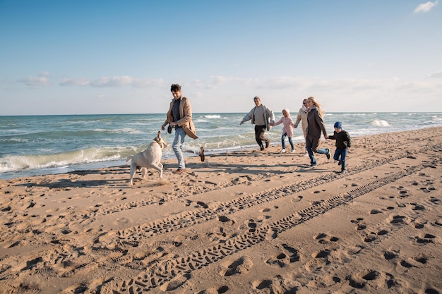 duża wielopokoleniowa rodzina biegająca z labradorem na plaży nad morzem