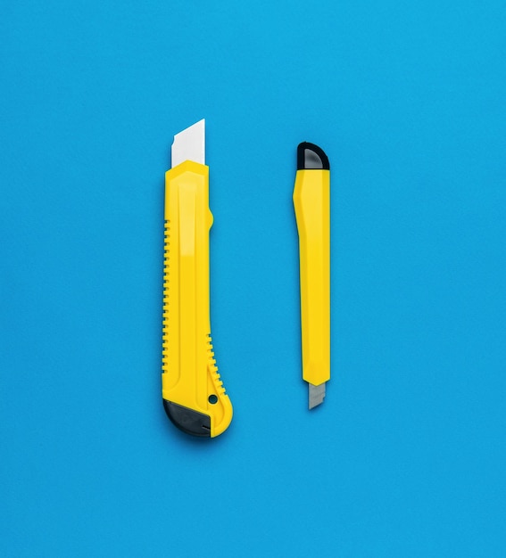Duże i małe żółte noże biurowe na niebieskim tle Narzędzia dla kreatywności i edukacji Płaski lay