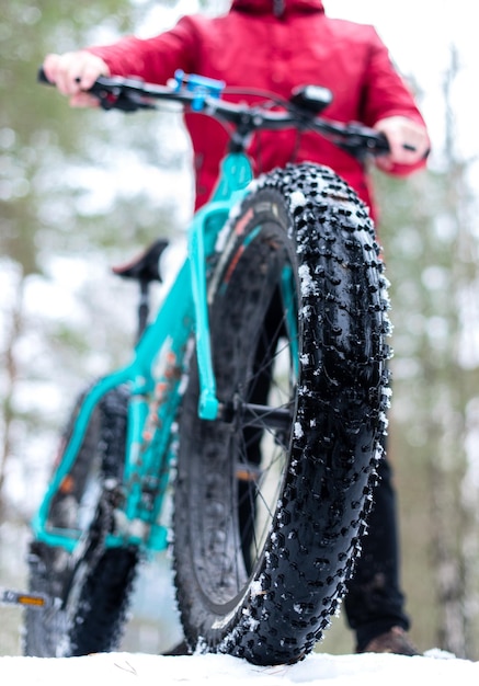 Duże koło od roweru Fatbike zimą w rękach mężczyzny w czerwonej kurtce