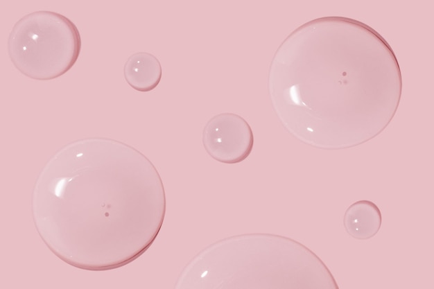 Duże krople żelu wodnego w płynie kosmetycznym na różowym tle