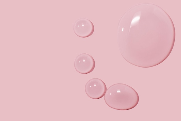 Duże krople żelu wodnego w płynie kosmetycznym na różowym tle