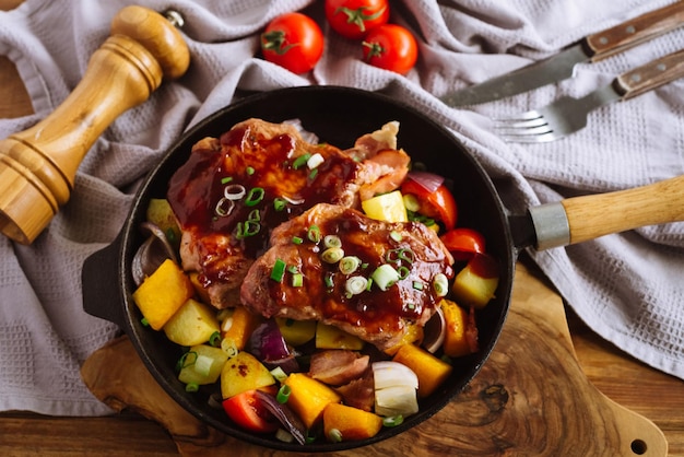 Duże steki wieprzowe wysmarowane sosem bbq spoczywają na dużych kawałkach warzyw na rycynowej patelni