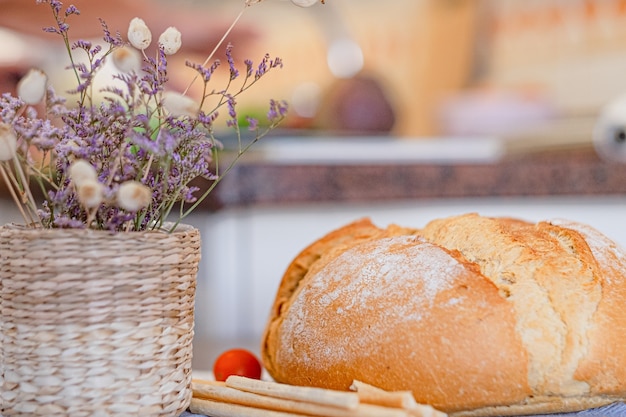 Duży bochenek chleba na domowym stole. Paluszki chlebowe, kosz suszonych kwiatów