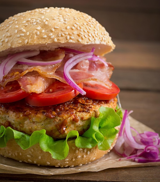 Duży hamburger z wołowiną, czerwoną cebulą, pomidorem i smażonym bekonem.