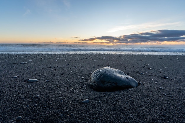 Duży izolowany czarny kamień pośrodku czarnej piaszczystej plaży Reynisfjara oświetlony