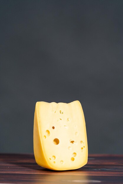 Duży kawałek półmiękkiego półtłustego szwajcarskiego sera na ciemnym drewnianym tle.