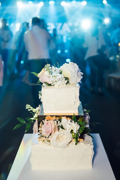 Zdjęcie duży kwadratowy tort weselny z trzema piętrami na tle oświetlenia ledowego ślub premium na ukrainie