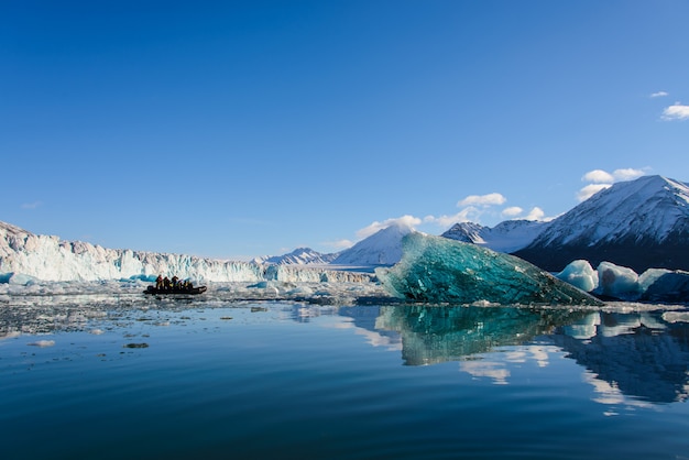 Duży niebieski kawałek lodu na morzu arktycznym. Ponton z turystami.