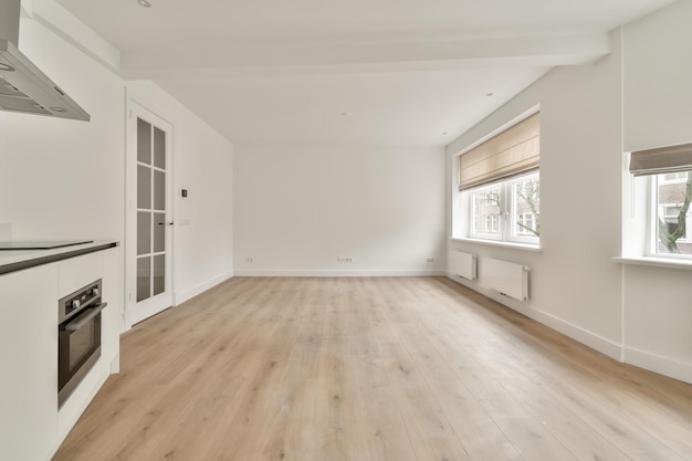 Duży pokój w pustym nowym domu z narożną kuchnią w minimalistycznym stylu wykonanym w bieli